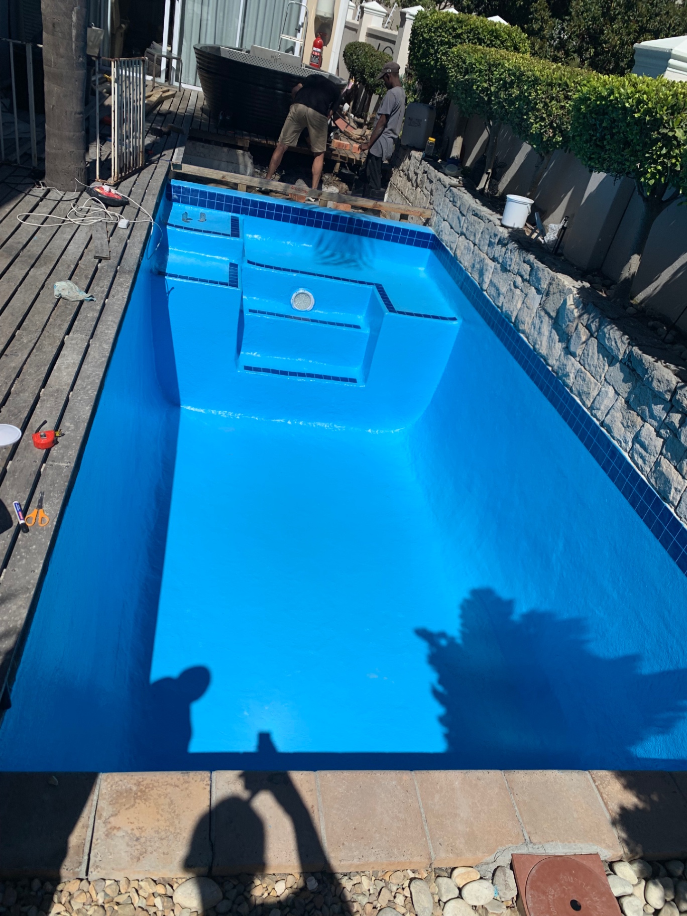 Freshly resurfaced bright blue pool shell with workers on site