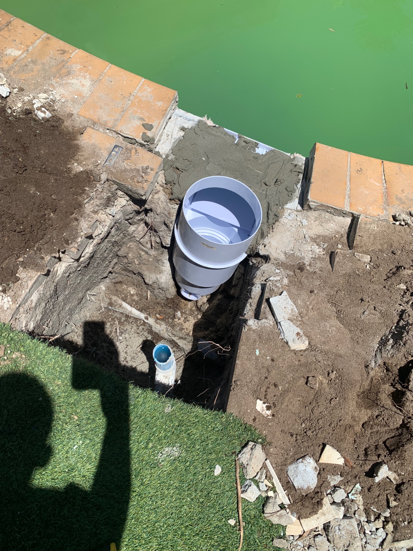 Careful excavation next to a pool wall to expose a leaking pipe fitting